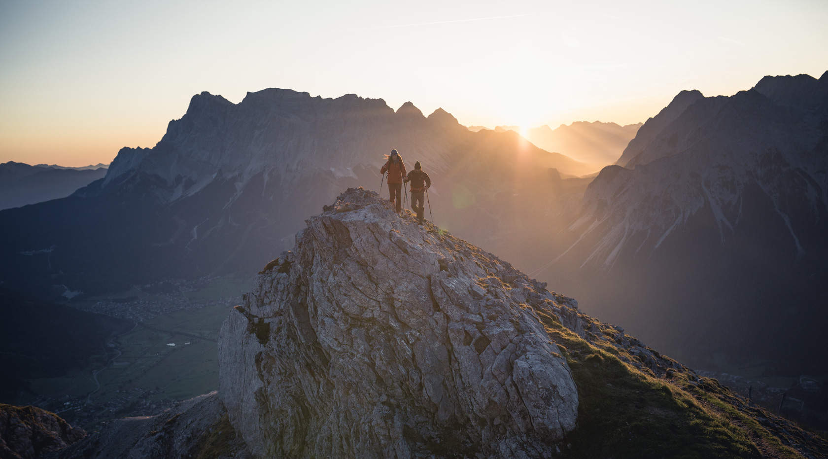 Ein Paar steht auf einem Gipfel bei Sonnenuntergang und genießt die Aussicht.