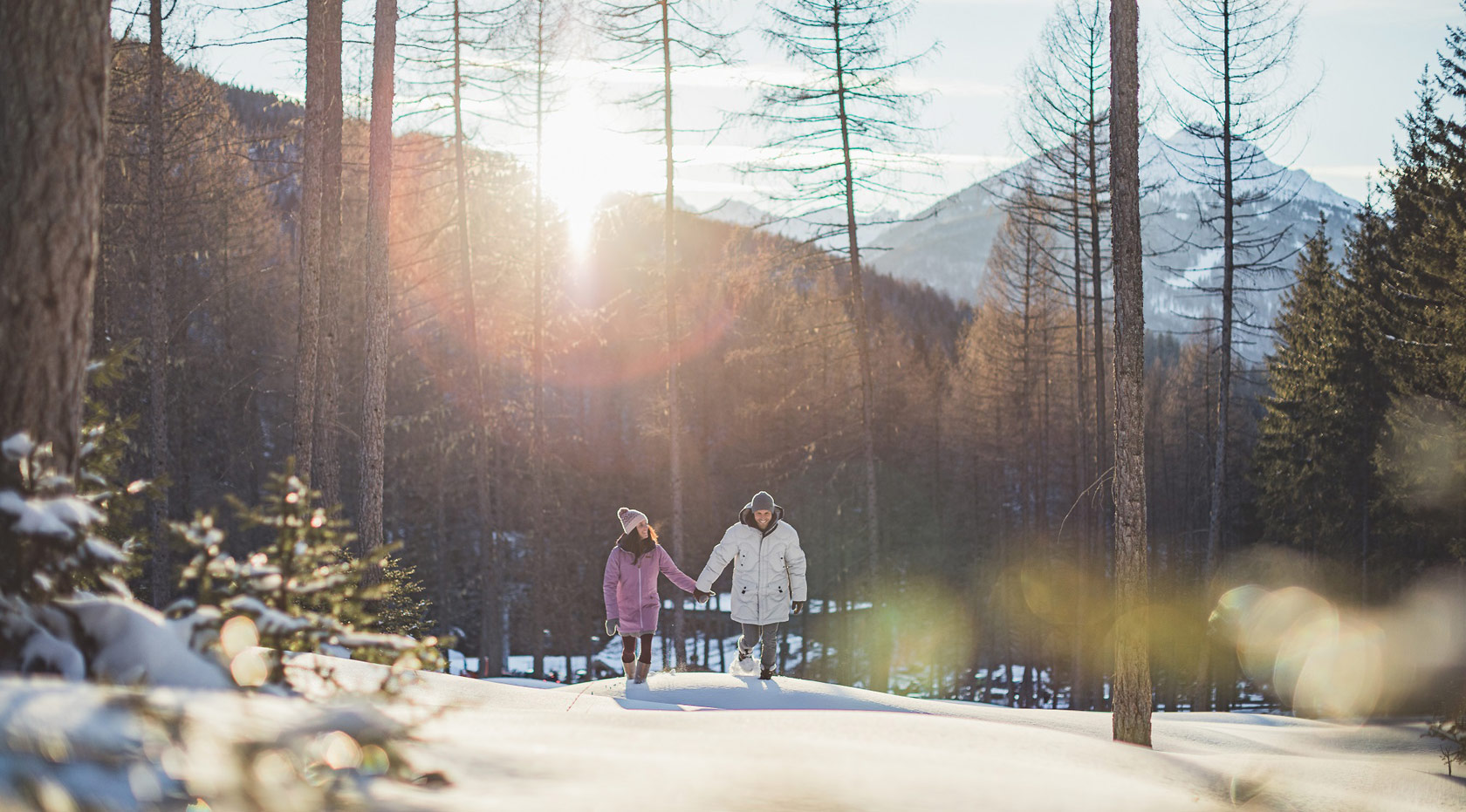 Paar wandert im Winter durch verschneiten Wald bei Sonnenlicht.